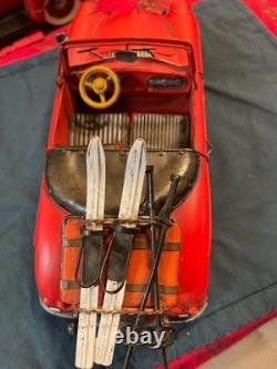 Vintage-style red tin toy car with skis and poles attached to the rear